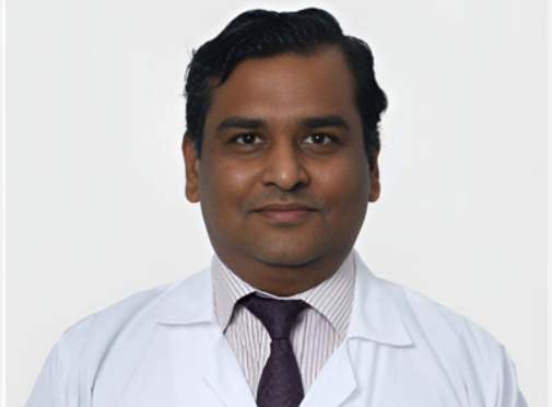 Portrait of a male doctor in a white coat and striped shirt against a light background.