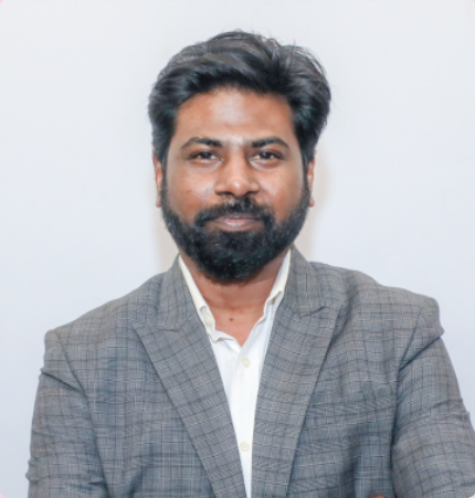 Picture1(39) Portrait of a man with a beard in a gray plaid blazer and white shirt, looking at the camera on a neutral background.