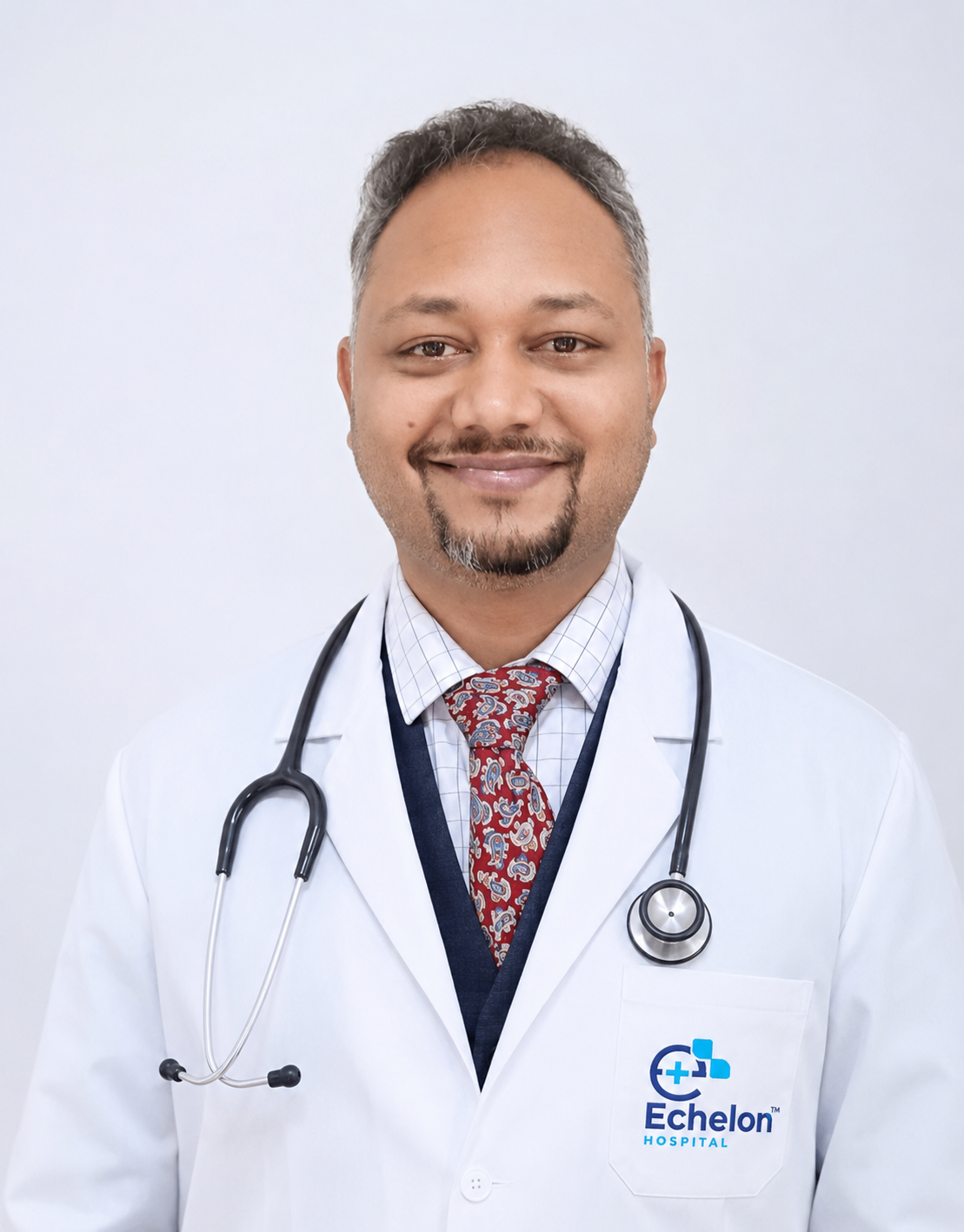 Male doctor in white coat with stethoscope, smiling, wearing a patterned tie; Echelon Hospital logo on coat pocket visible.