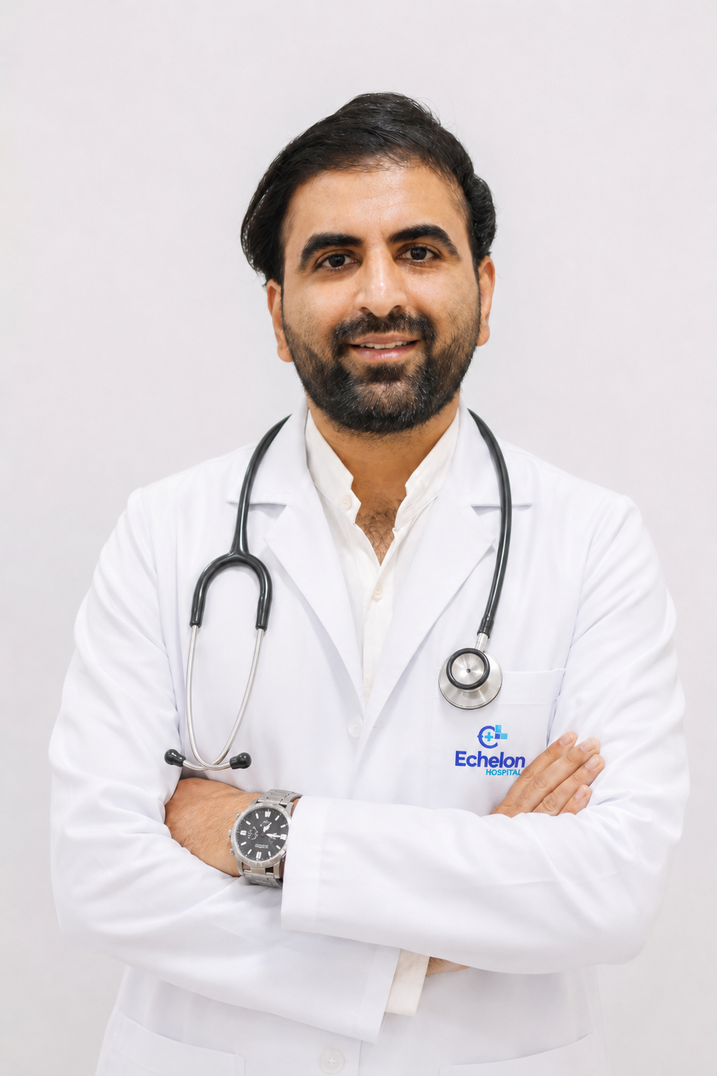 Male doctor in a white lab coat with a stethoscope around his neck, arms crossed, smiling against a light background, Echelon Hospital logo on coat