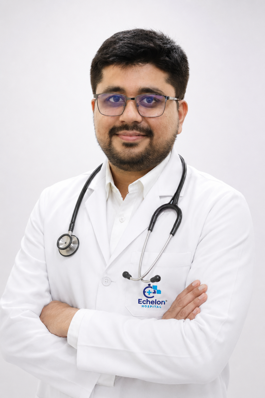 Male doctor in a white coat with stethoscope, arms crossed, wearing glasses, at Echelon Hospital.
