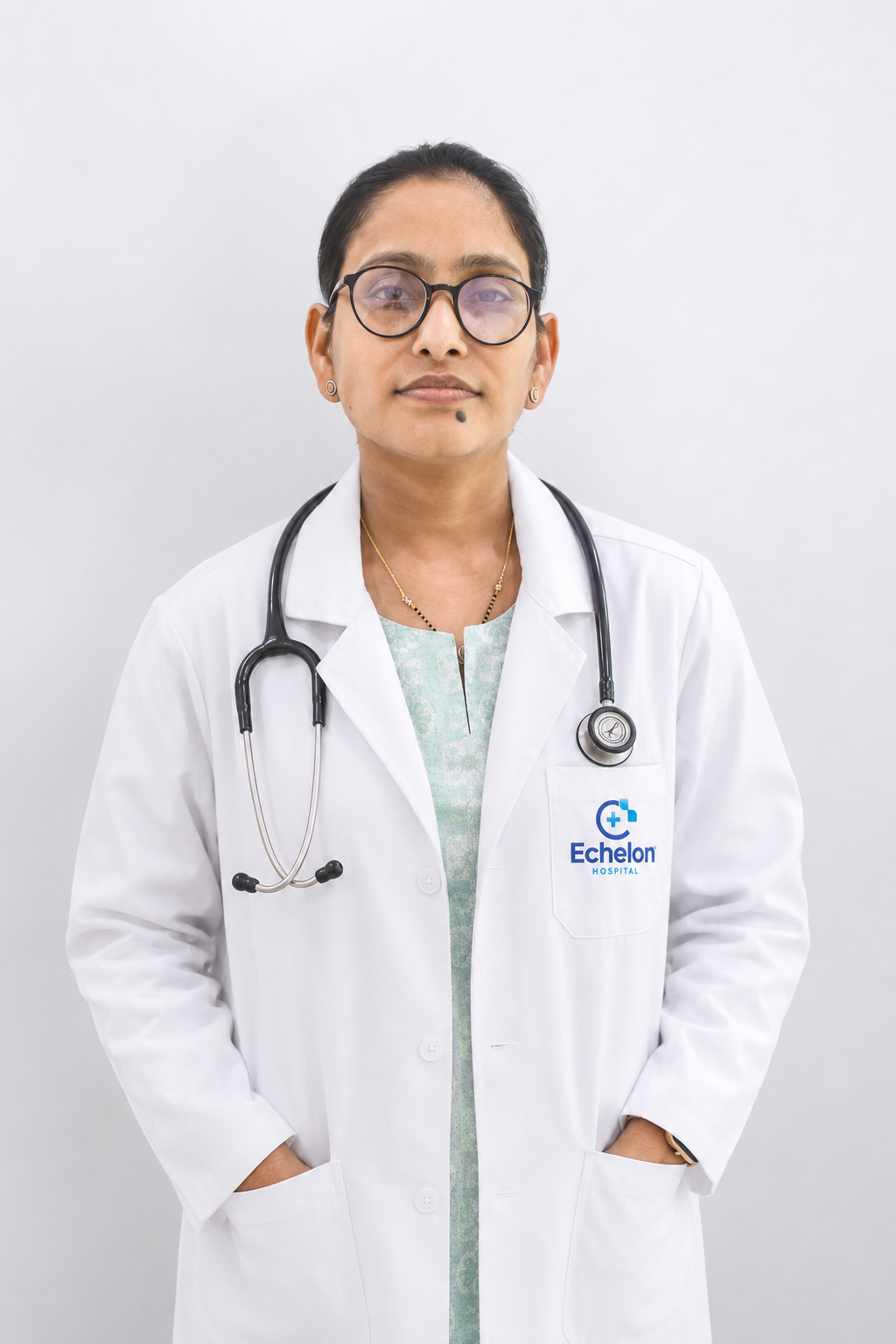 Female doctor in white coat with stethoscope, hands in pockets, Echelon Hospital logo on pocket.