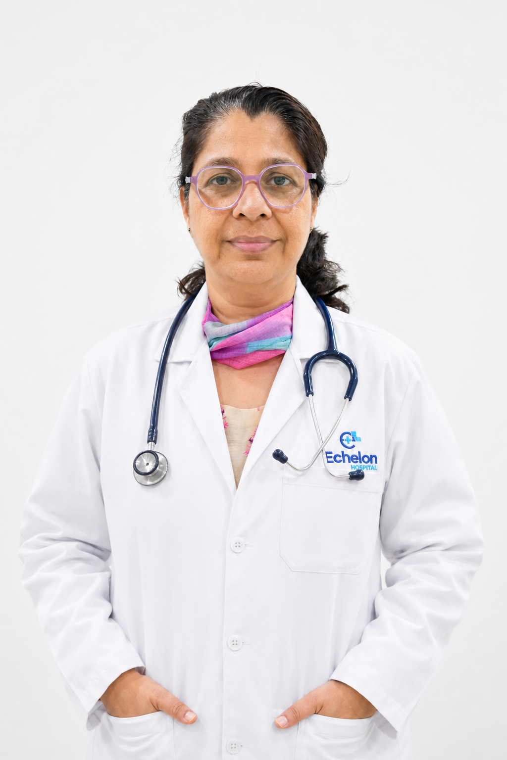 Female doctor with purple glasses and a stethoscope, wearing a white coat with Echelon Hospital logo, standing against a plain background.
