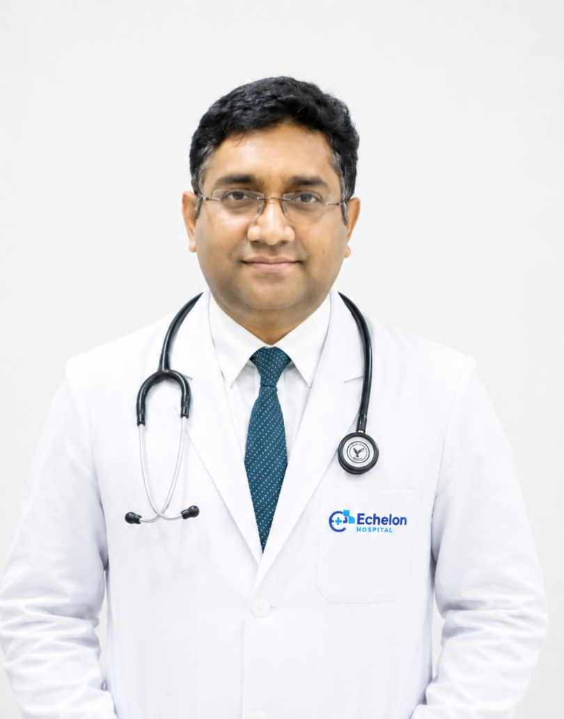 Male doctor in a white coat with stethoscope around the neck, standing against a light background; Echelon Hospital logo on pocket.