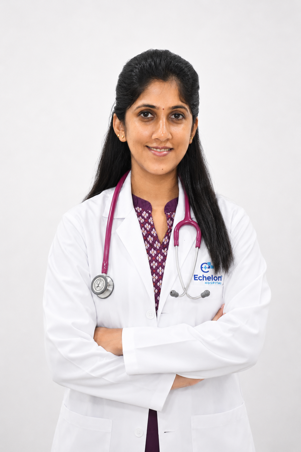 DR.SONIA SREENIVAS Professional portrait of a female doctor wearing a white coat and stethoscope, arms crossed, looking at the camera.