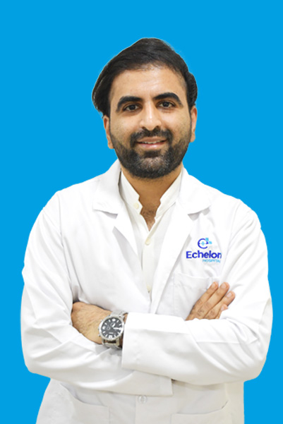Male doctor in a white lab coat with arms crossed, smiling, against a solid blue background; coat bears an Echelon logo on the left chest.