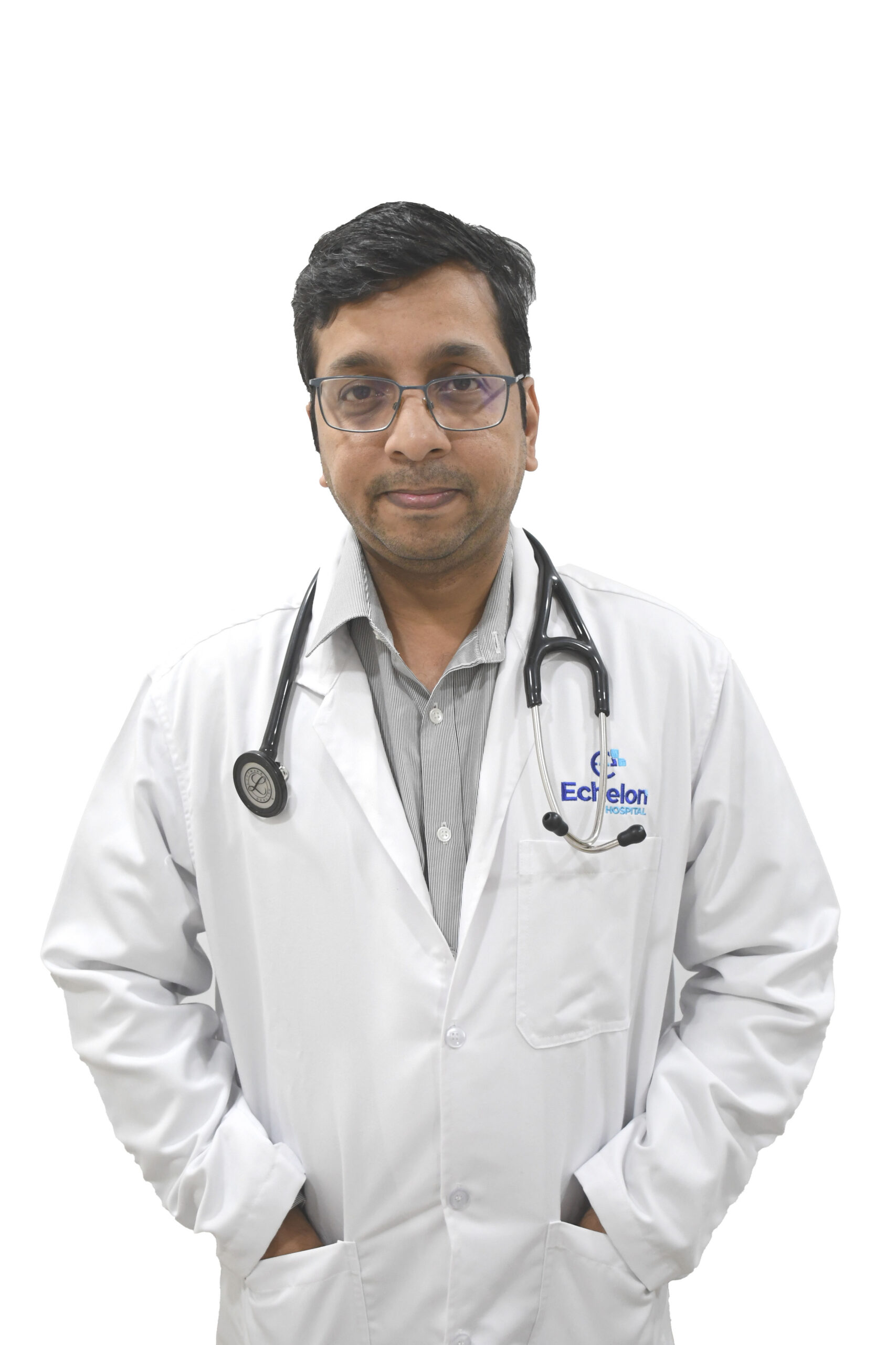 Male doctor in a white coat with a stethoscope around his neck, standing with hands in pockets against a white background.