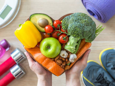 Hands hold a heart-shaped tray of fresh vegetables and nuts, symbolizing healthy eating.