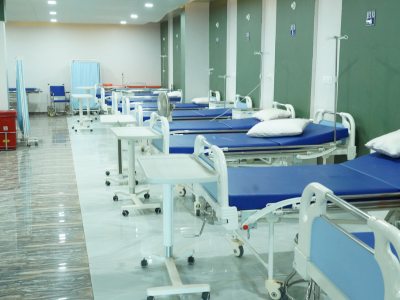 Row of hospital beds with blue mattresses and white rails in a clean, well-lit ward.
