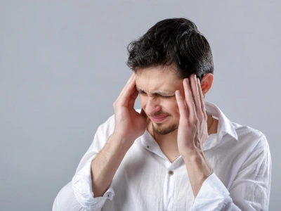 Man in a white shirt rubbing his temples, showing a headache or stress attraction.
