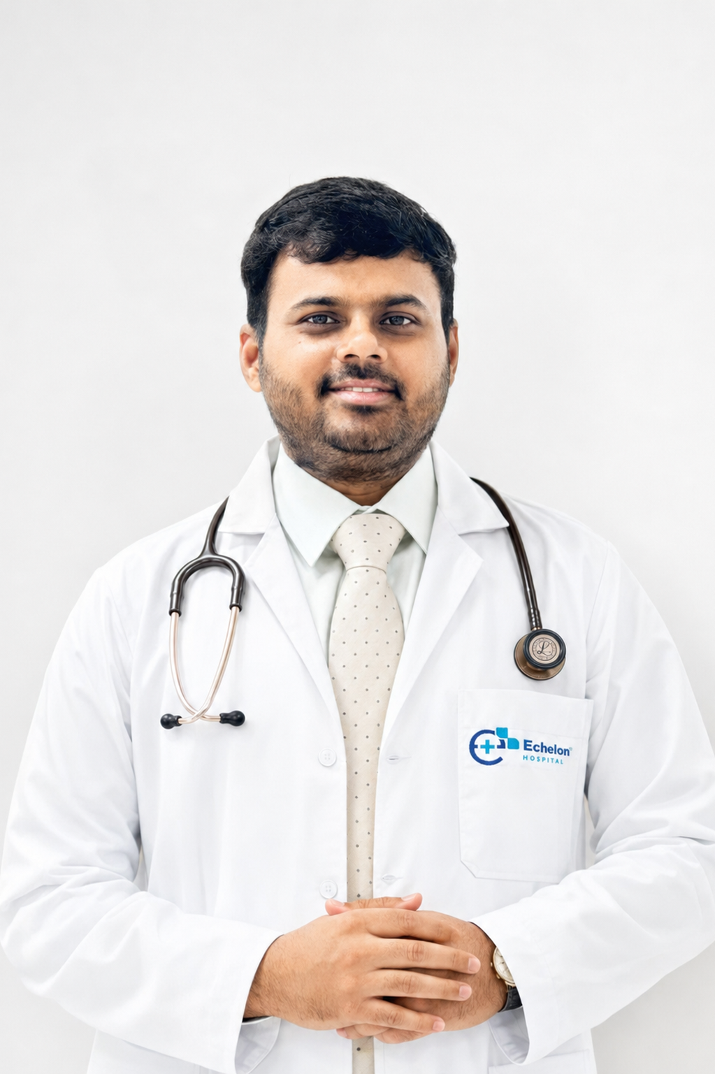 Male doctor in a white coat with stethoscope, standing against a light background, pocket badge reads Echelon Hospital.