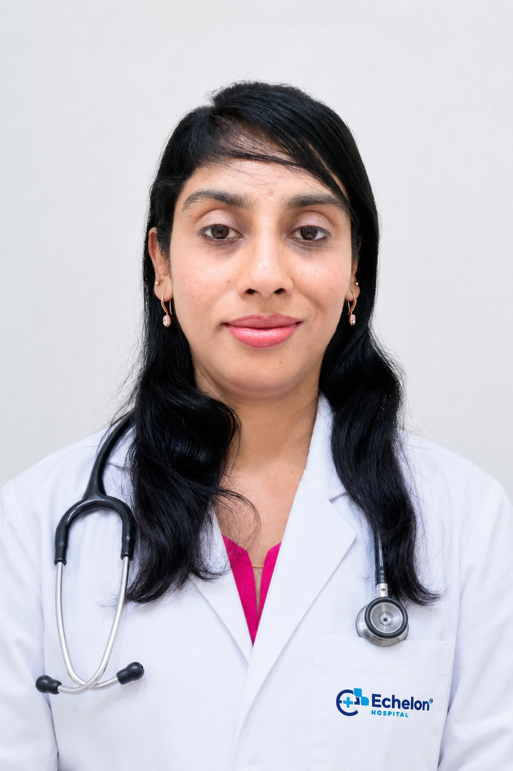 Portrait of a female doctor in a white coat with a stethoscope, smiling, against a light gray background; Echelon Hospital logo on the pocket.