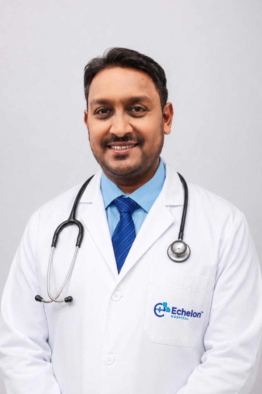 Smiling male doctor in a white coat with blue tie and stethoscope, Echelon Hospital logo on his pocket.